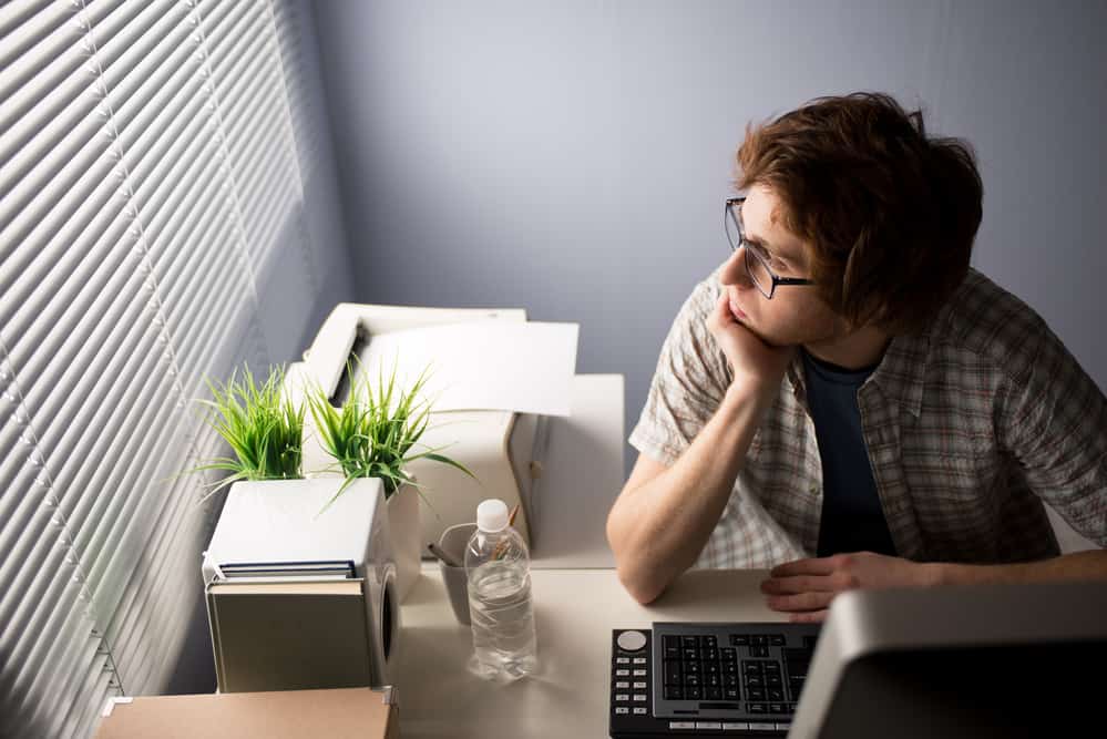 Young bored guy at office looking at window with pensive expression.